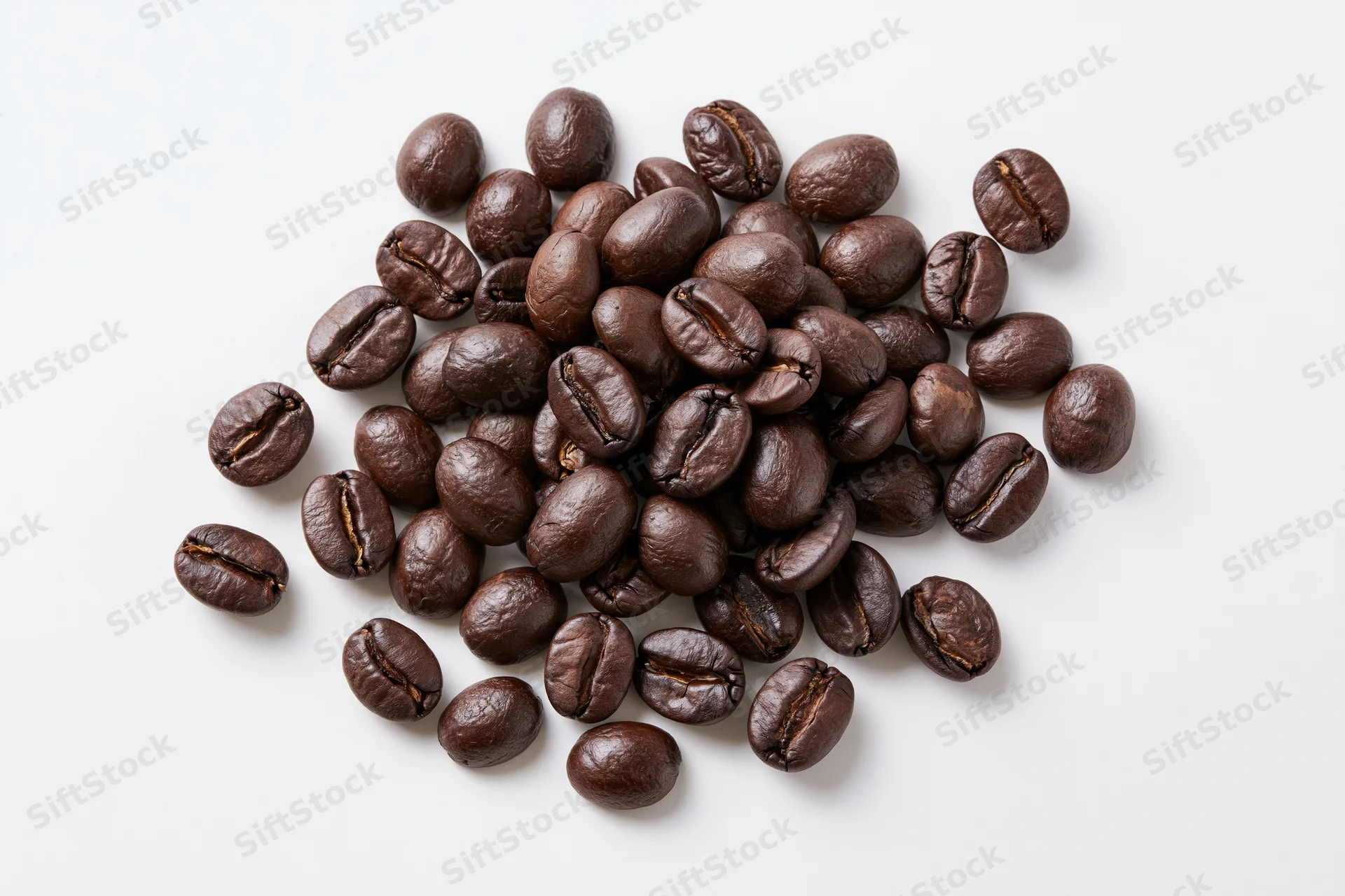 Dark roasted coffee beans scattered in a loose pile on a white surface