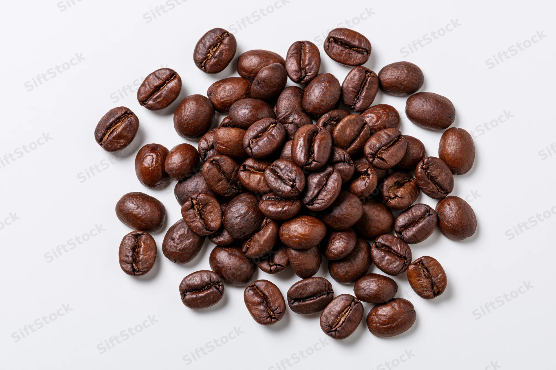 Dark roasted coffee beans scattered loosely on a white surface