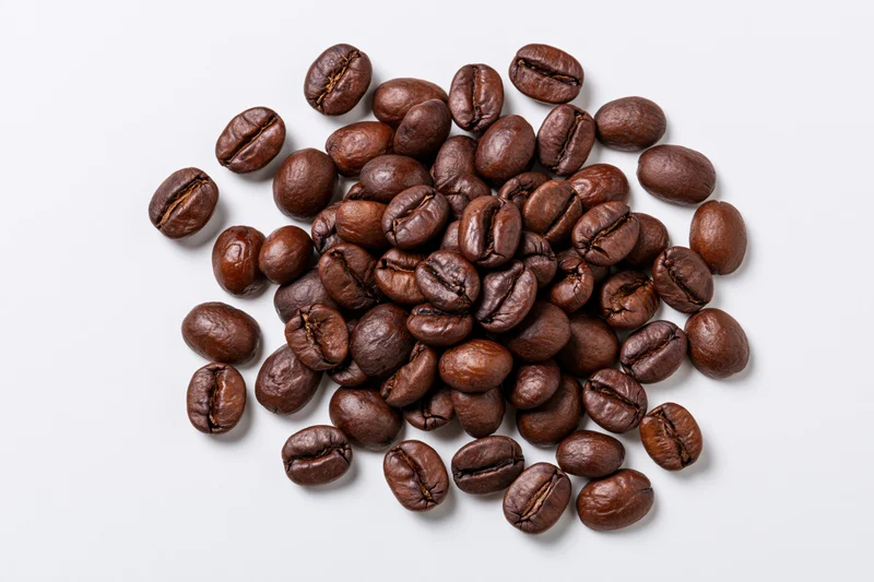 Dark roasted coffee beans scattered loosely on a white surface