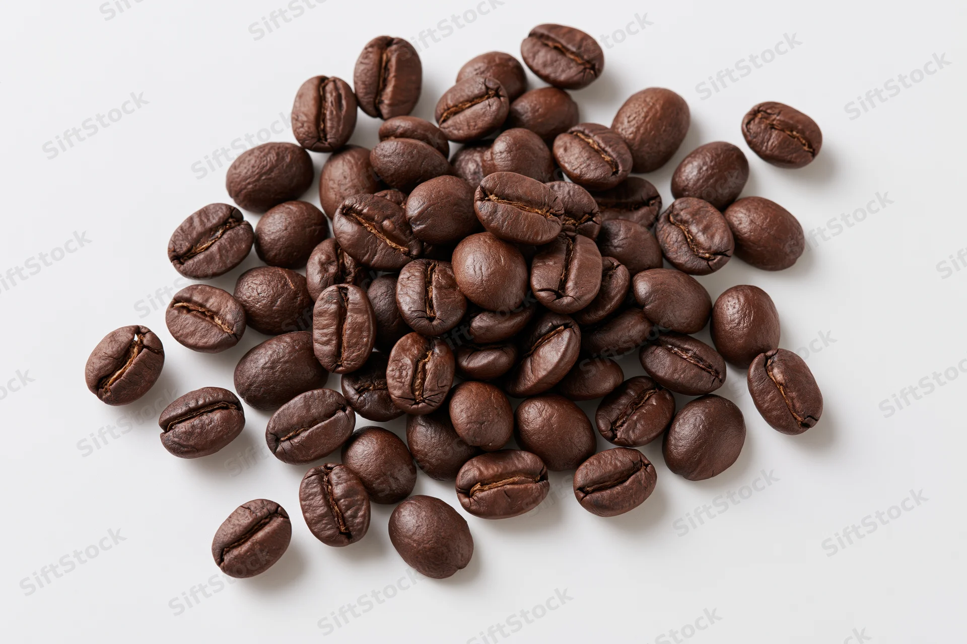 Dark roasted coffee beans scattered loosely on a white surface
