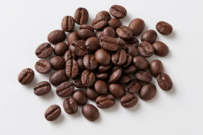 Dark roasted coffee beans scattered loosely on a white surface