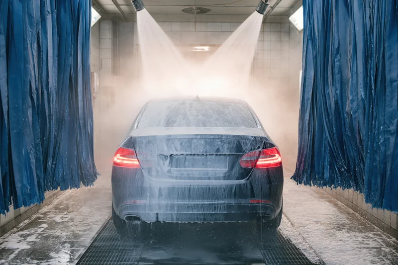 Dark sedan being sprayed with water and foam inside an automatic car wash tunnel