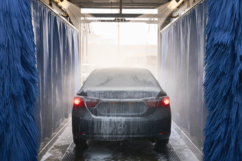 Dark sedan covered in foam and water spray inside automatic car wash tunnel
