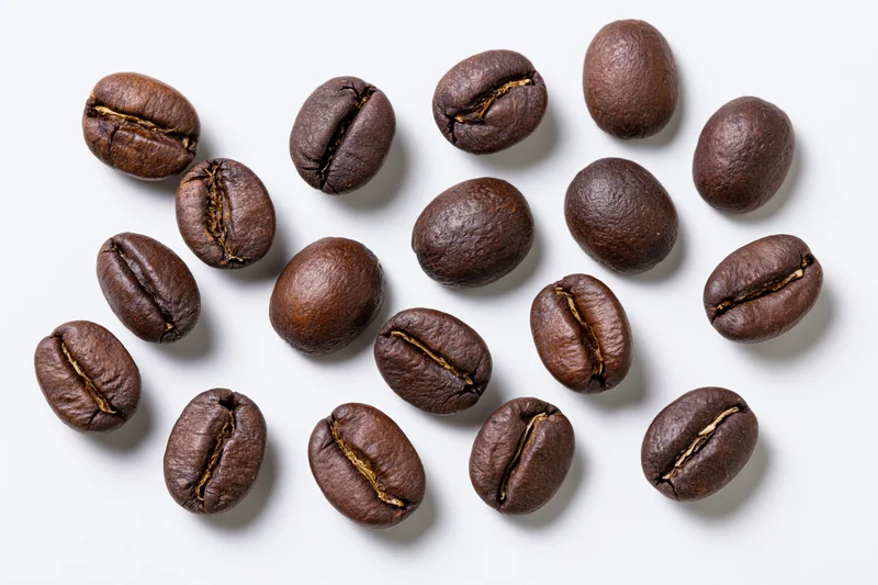 Roasted coffee beans scattered across a white background in a top-down closeup view