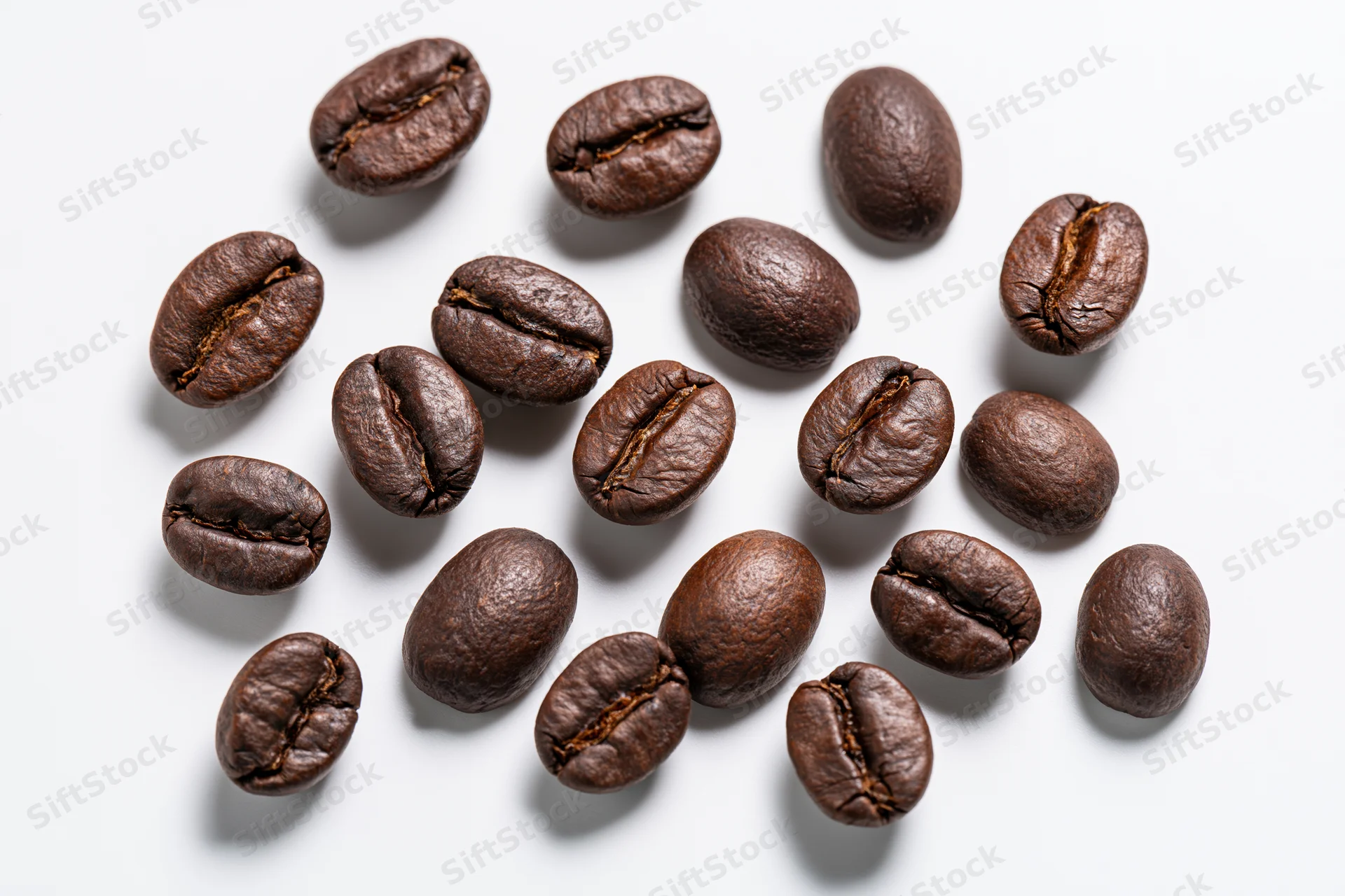 Roasted coffee beans scattered across a white background in a close-up top view