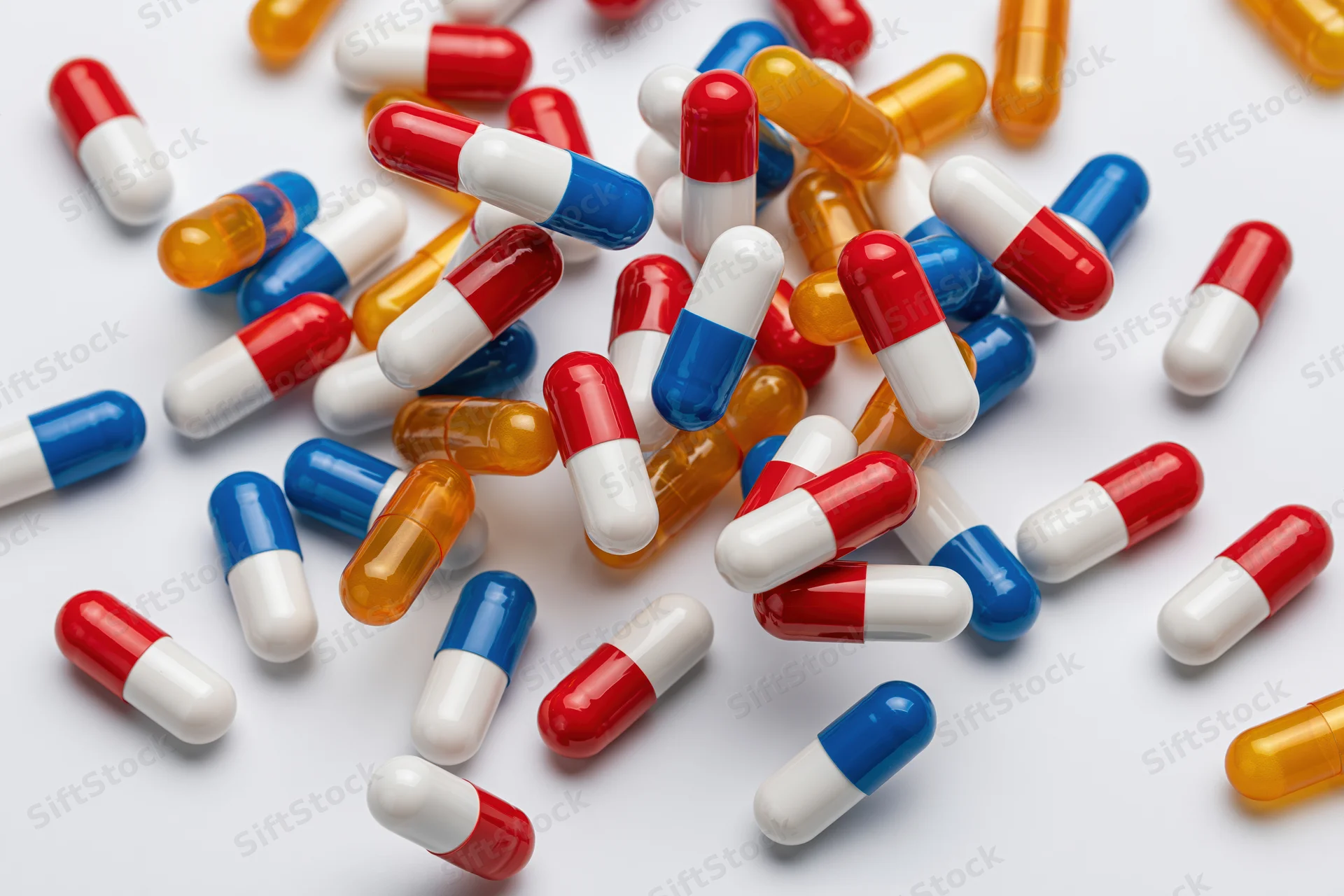 Scattered pharmaceutical capsules in red, white, blue and orange on a white surface