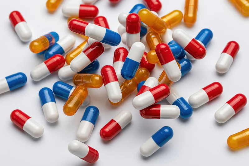 Scattered pharmaceutical capsules in red, white, blue and orange on a white surface