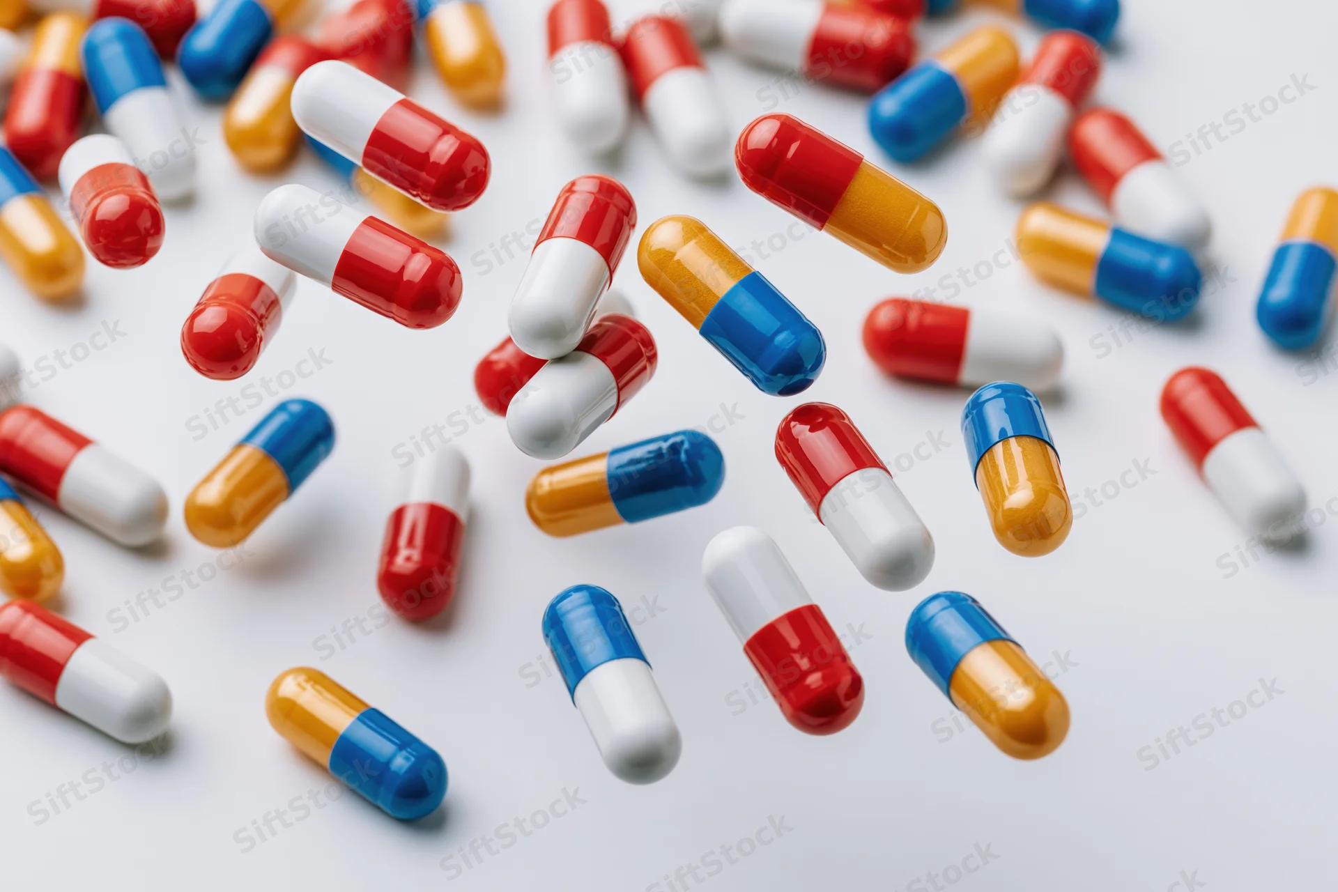 Scattered pharmaceutical capsules in red, white, blue, and orange on a light surface