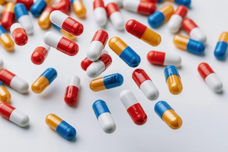 Scattered pharmaceutical capsules in red, white, blue, and orange on a light surface