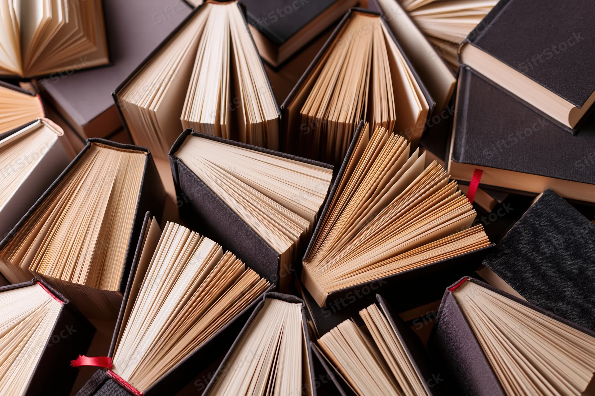 Dozens of hardcover books standing upright and scattered with pages fanned open, some marked with red ribbons