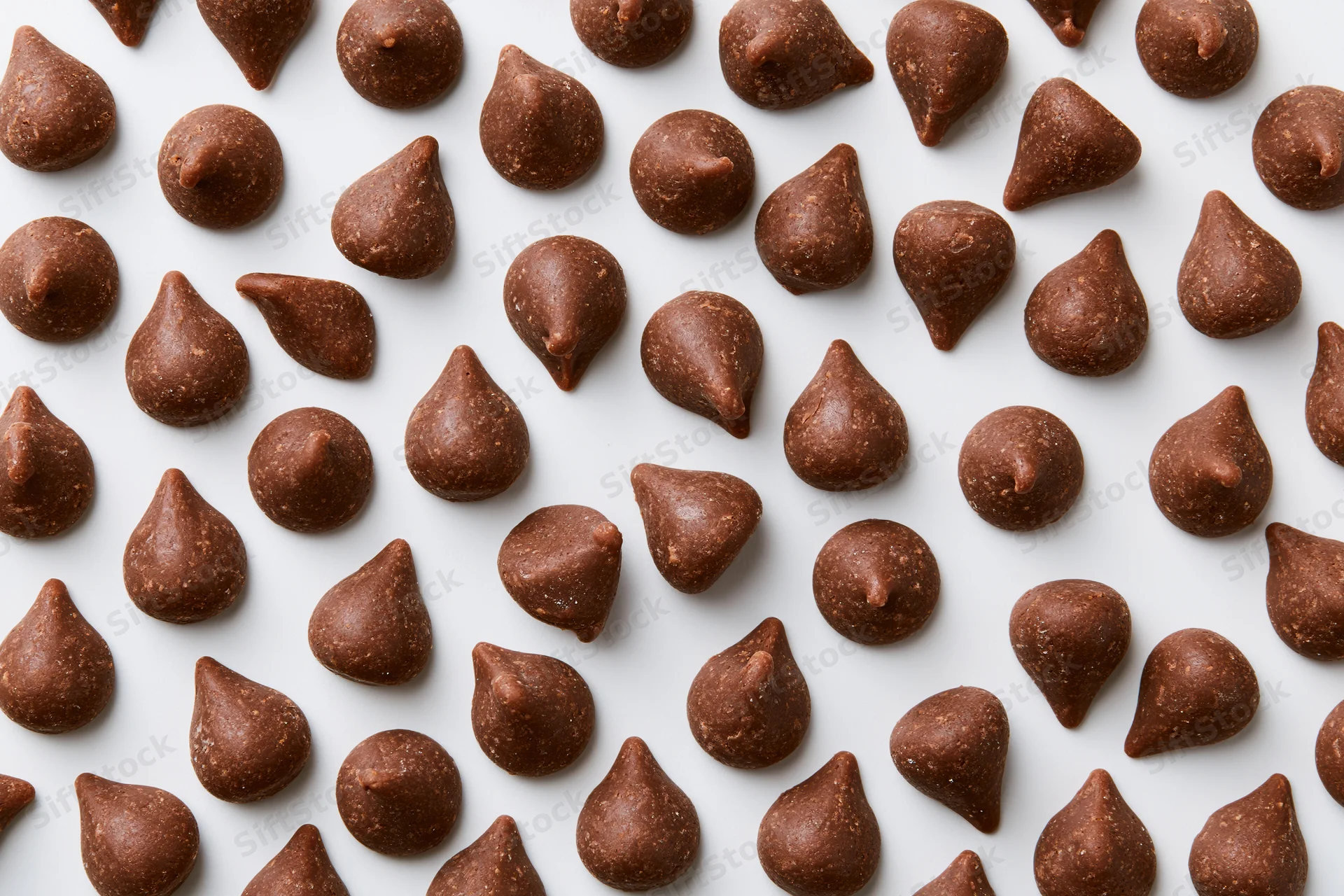 Chocolate chips scattered randomly across a white surface in a flat lay arrangement