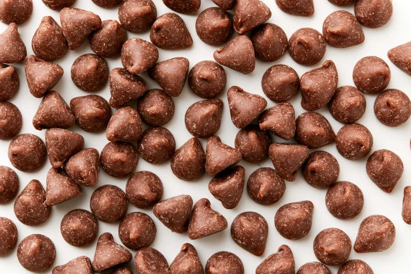 Chocolate chips scattered across a white surface in a close-up still life view