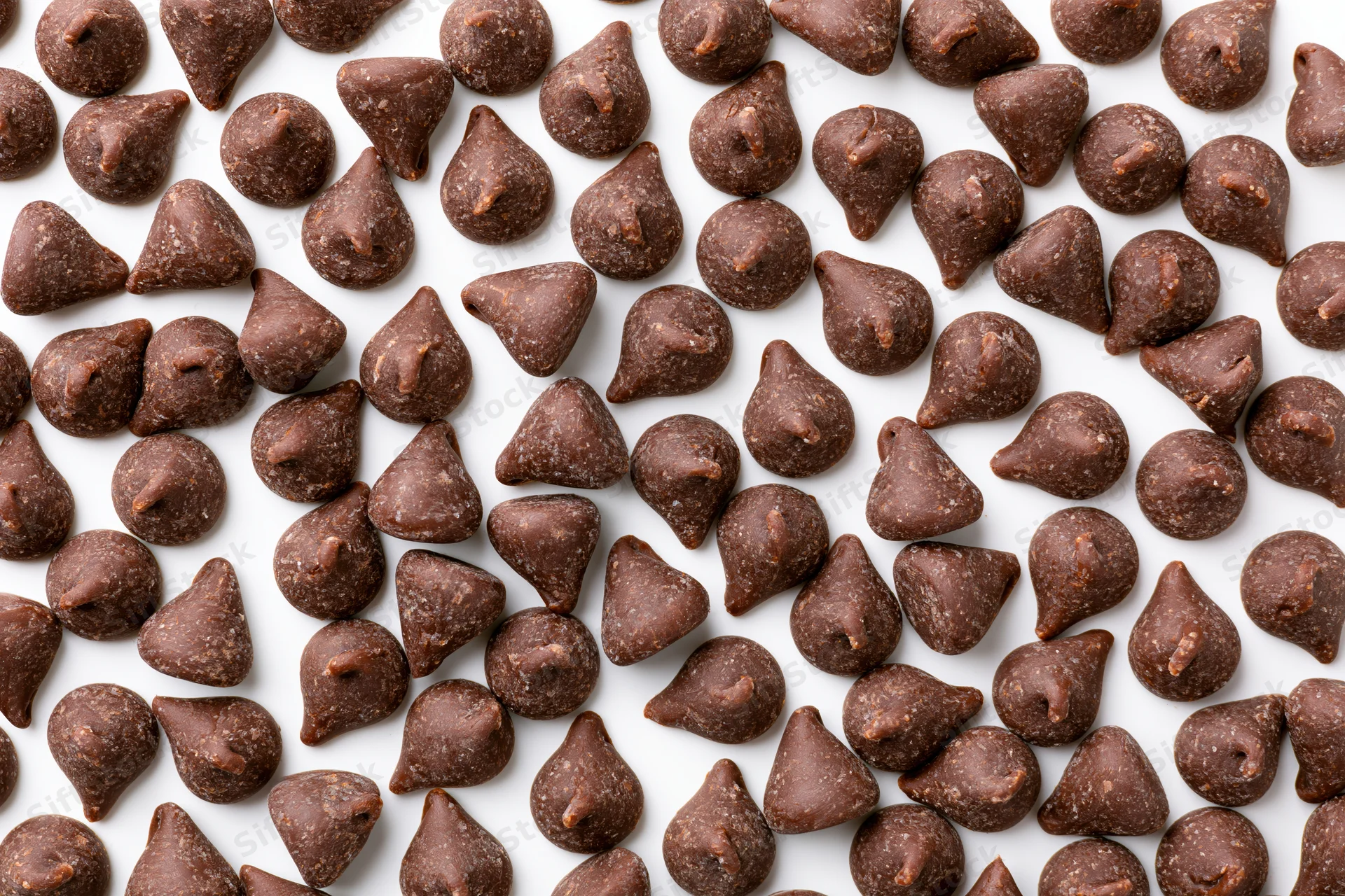 Chocolate chips scattered across white surface in flat lay top view