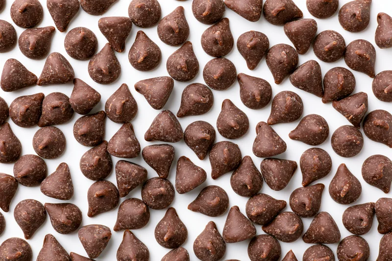 Chocolate chips scattered across white surface in flat lay top view