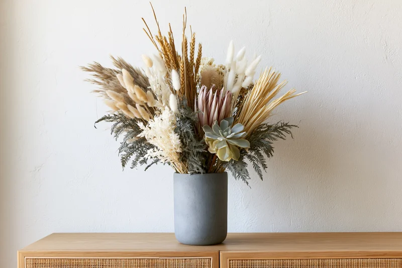 Dried flower arrangement in a matte grey ceramic cylinder vase on a wooden cabinet
