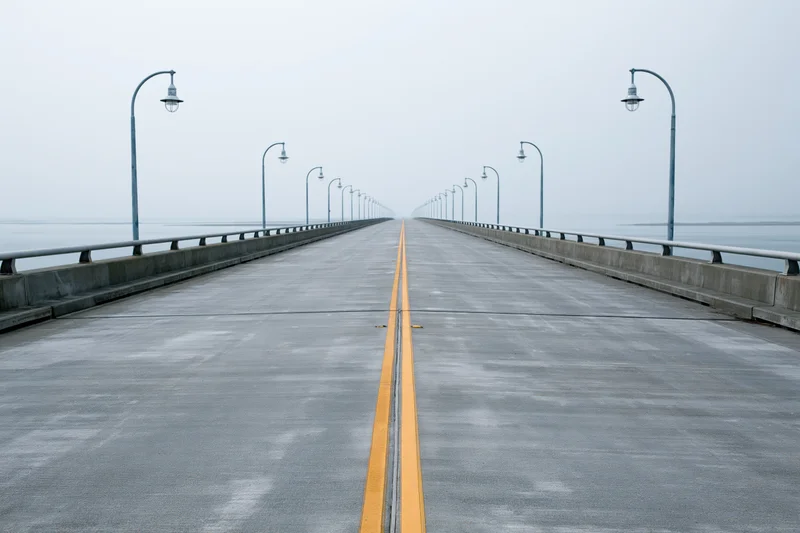Empty concrete highway bridge stretching toward the horizon over water in fog