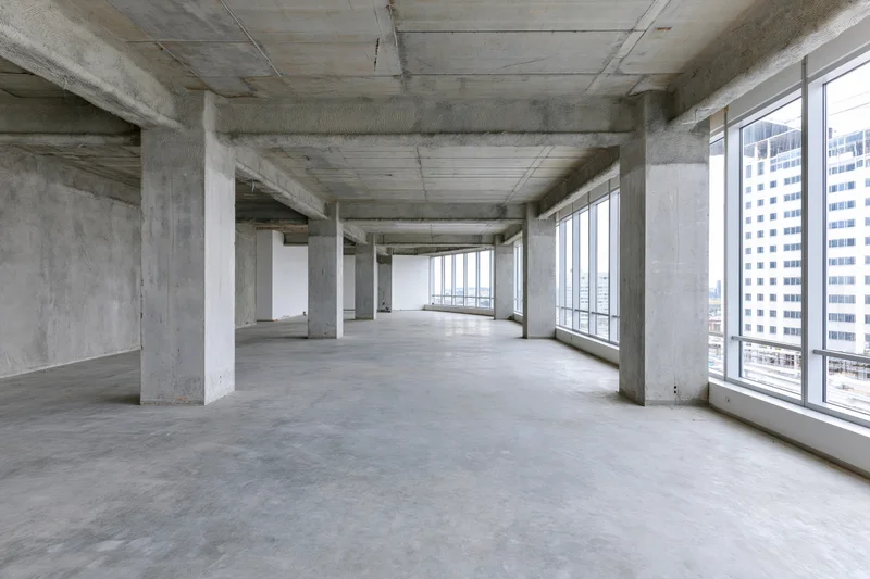 Empty unfinished concrete office space with large windows overlooking city buildings