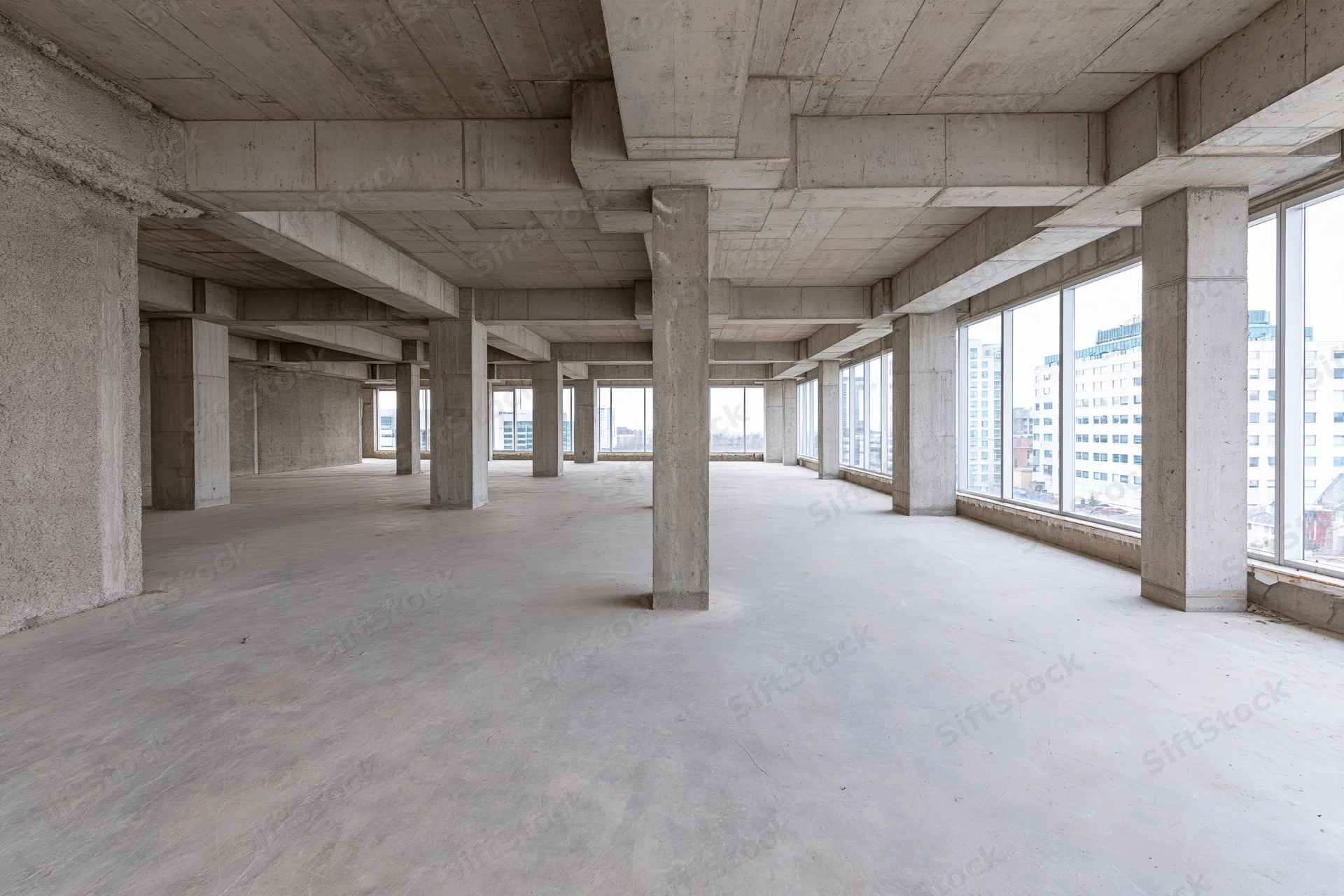 Empty concrete interior with pillars and windows overlooking city buildings