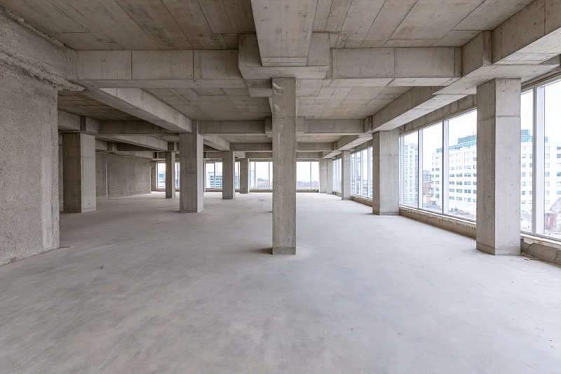 Empty concrete interior with pillars and windows overlooking city buildings