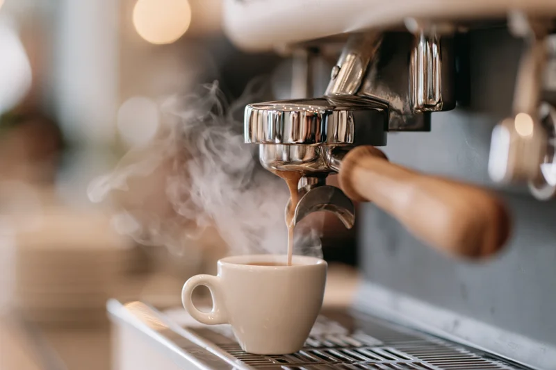 Espresso machine extracting shot into small white ceramic cup on metal drip tray in cafe