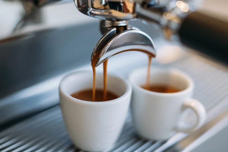 Espresso machine portafilter pouring coffee into two white cups on a metal drip tray