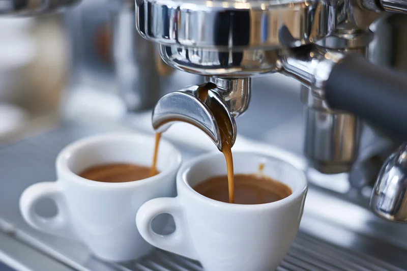 Espresso machine portafilter pouring coffee into two white cups on a metal tray