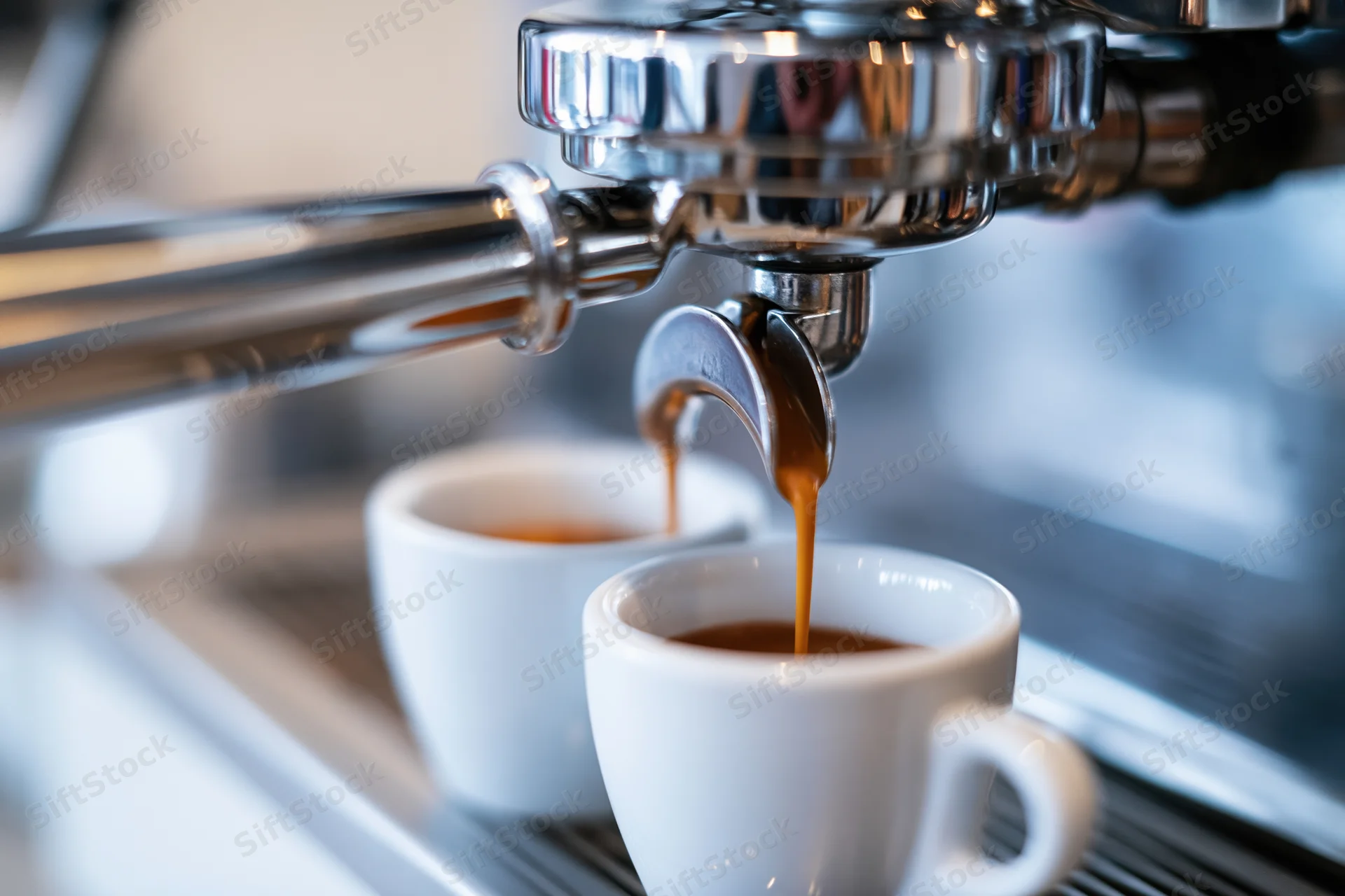 Espresso machine portafilter pouring coffee into two white cups on a metal counter