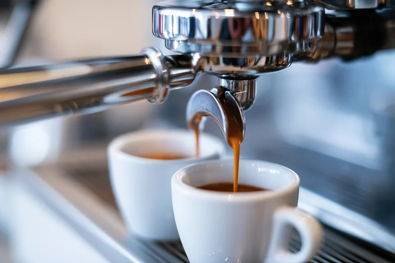 Espresso machine portafilter pouring coffee into two white cups on a metal counter