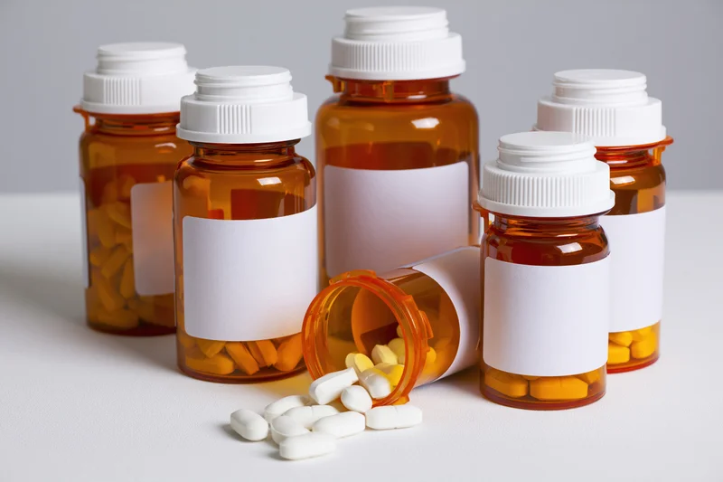 Amber prescription bottles with white labels and scattered pills on white surface