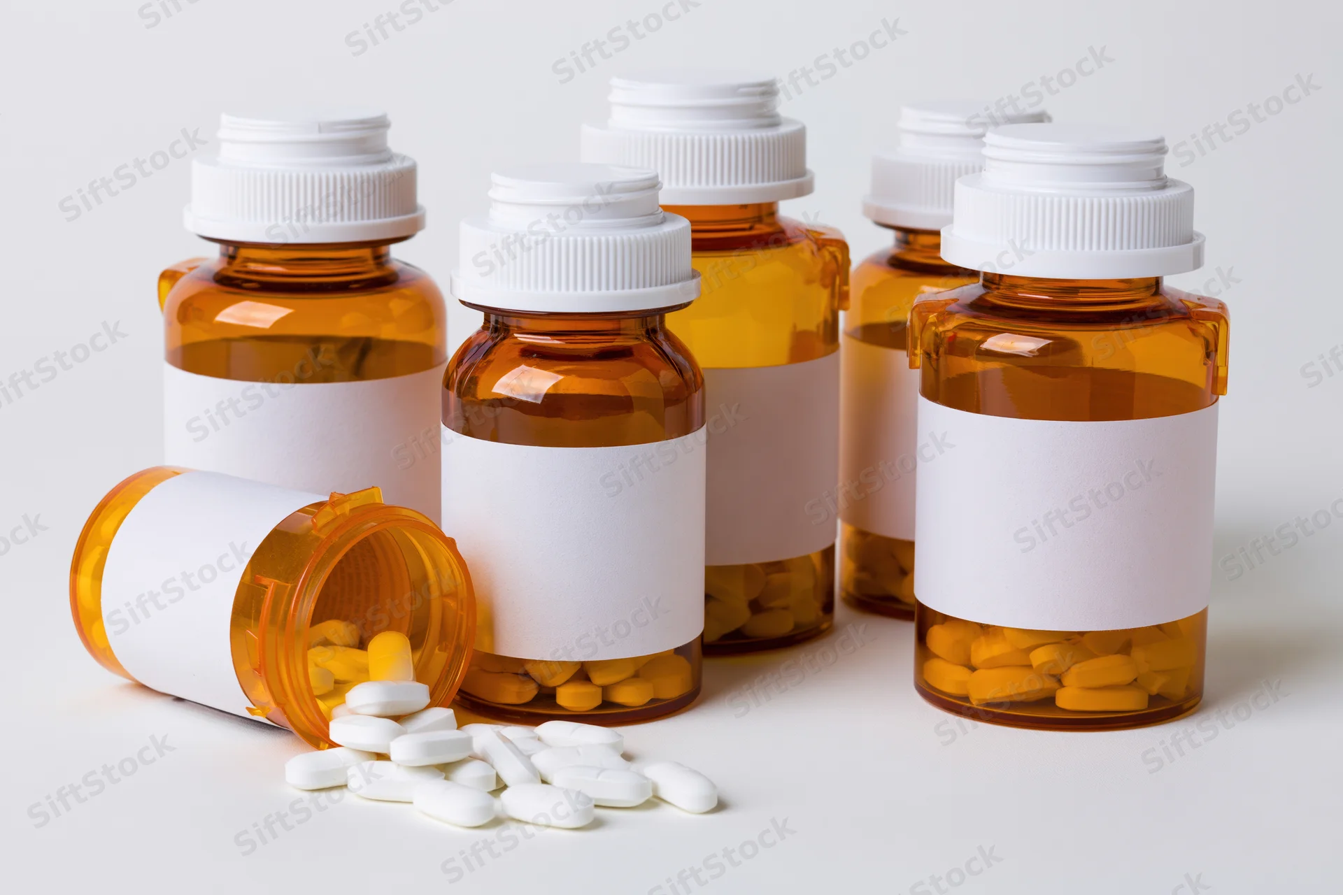 Amber prescription bottles with white labels and scattered pills on white background