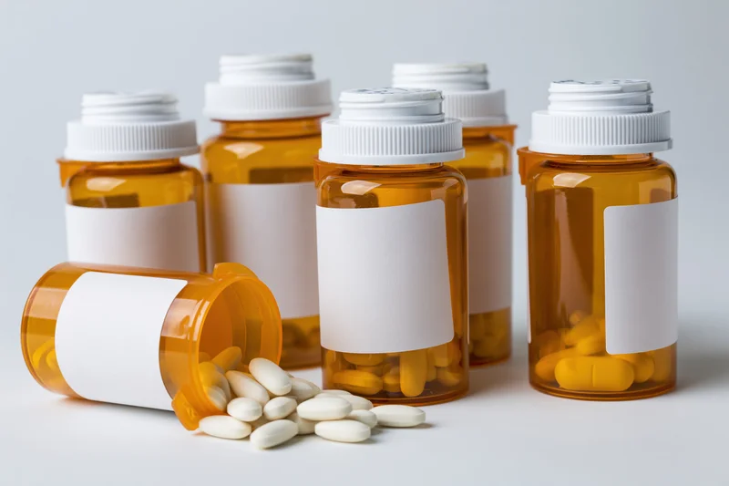 Amber prescription bottles with blank labels and scattered pills on white surface