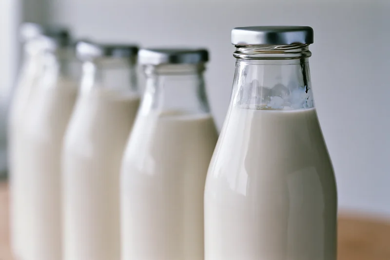 Row of glass milk bottles filled with fresh whole milk on wooden surface