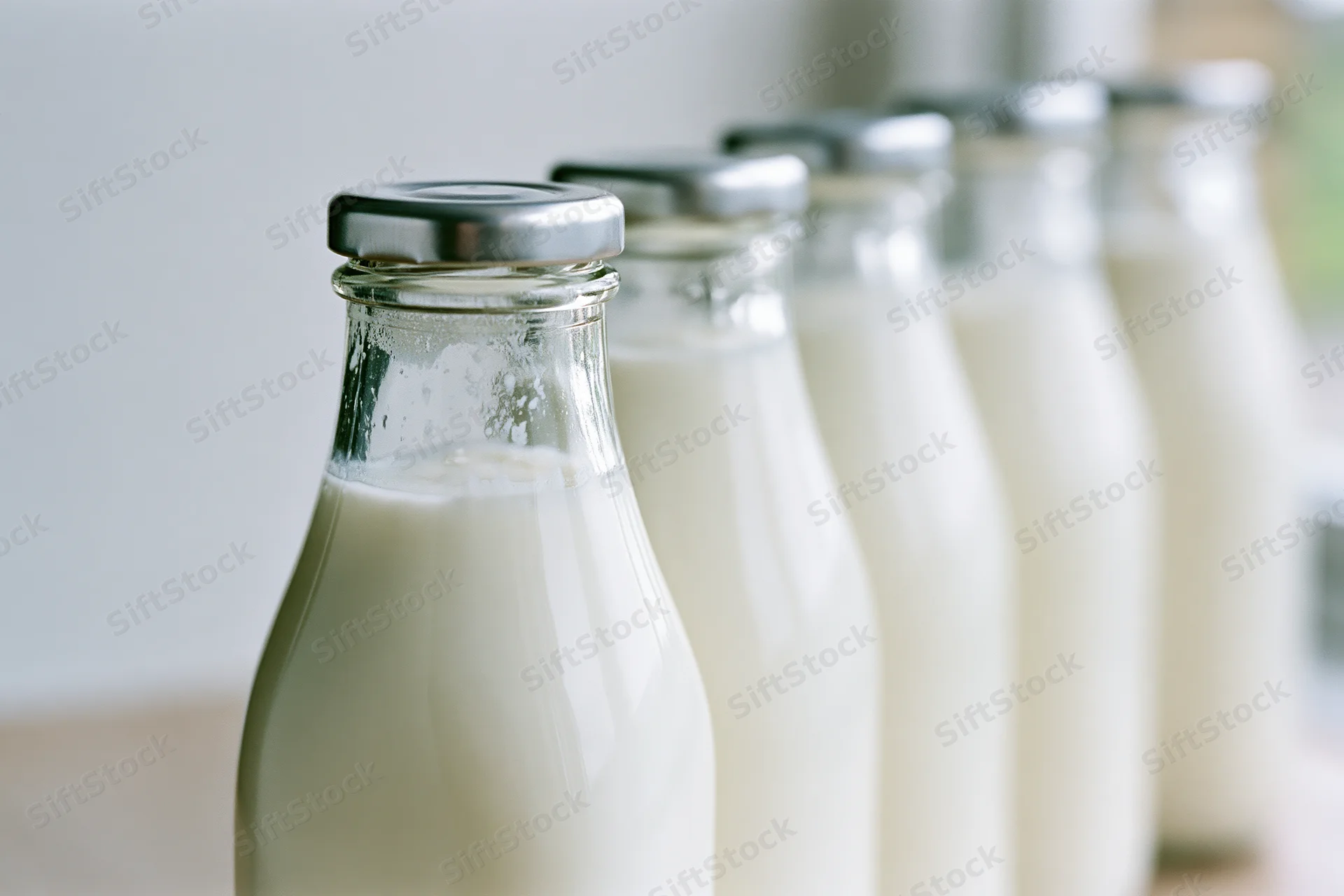 Row of glass milk bottles filled with fresh whole milk on a kitchen surface