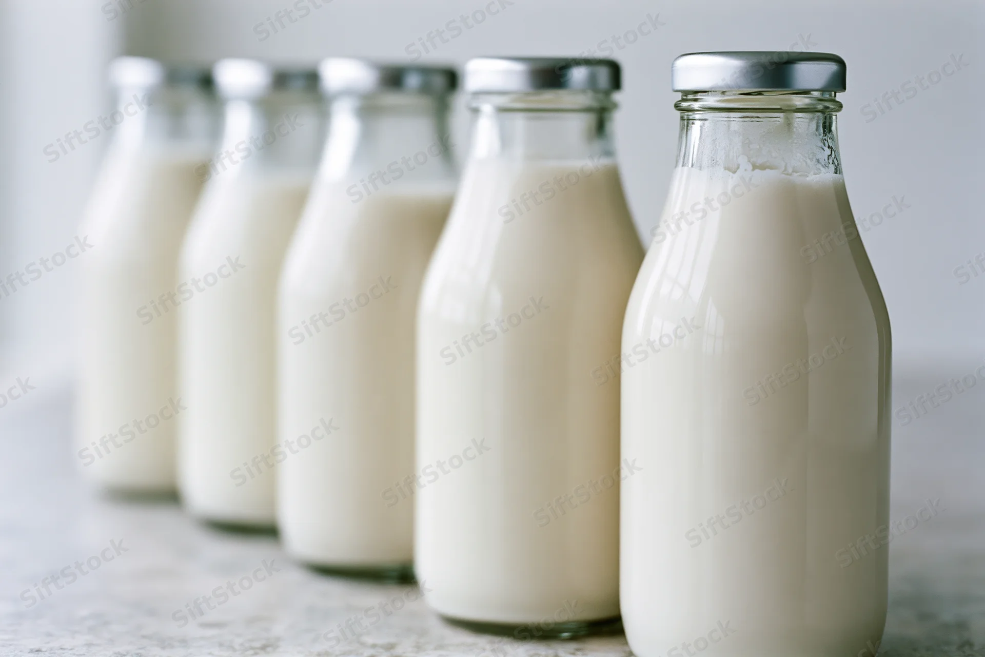 Five glass bottles filled with milk lined up on a countertop