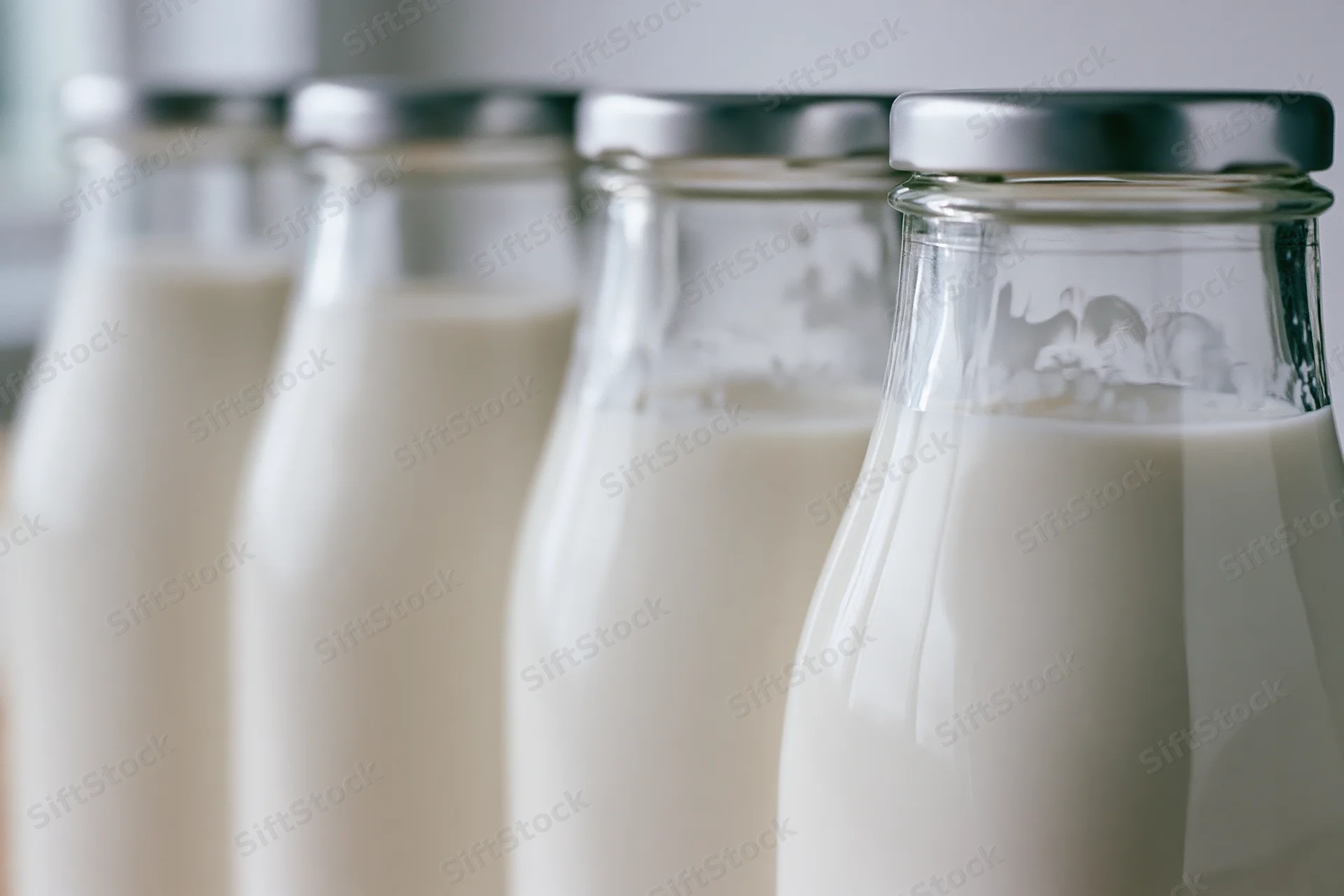 Row of glass milk bottles filled with fresh whole milk lined up on a surface