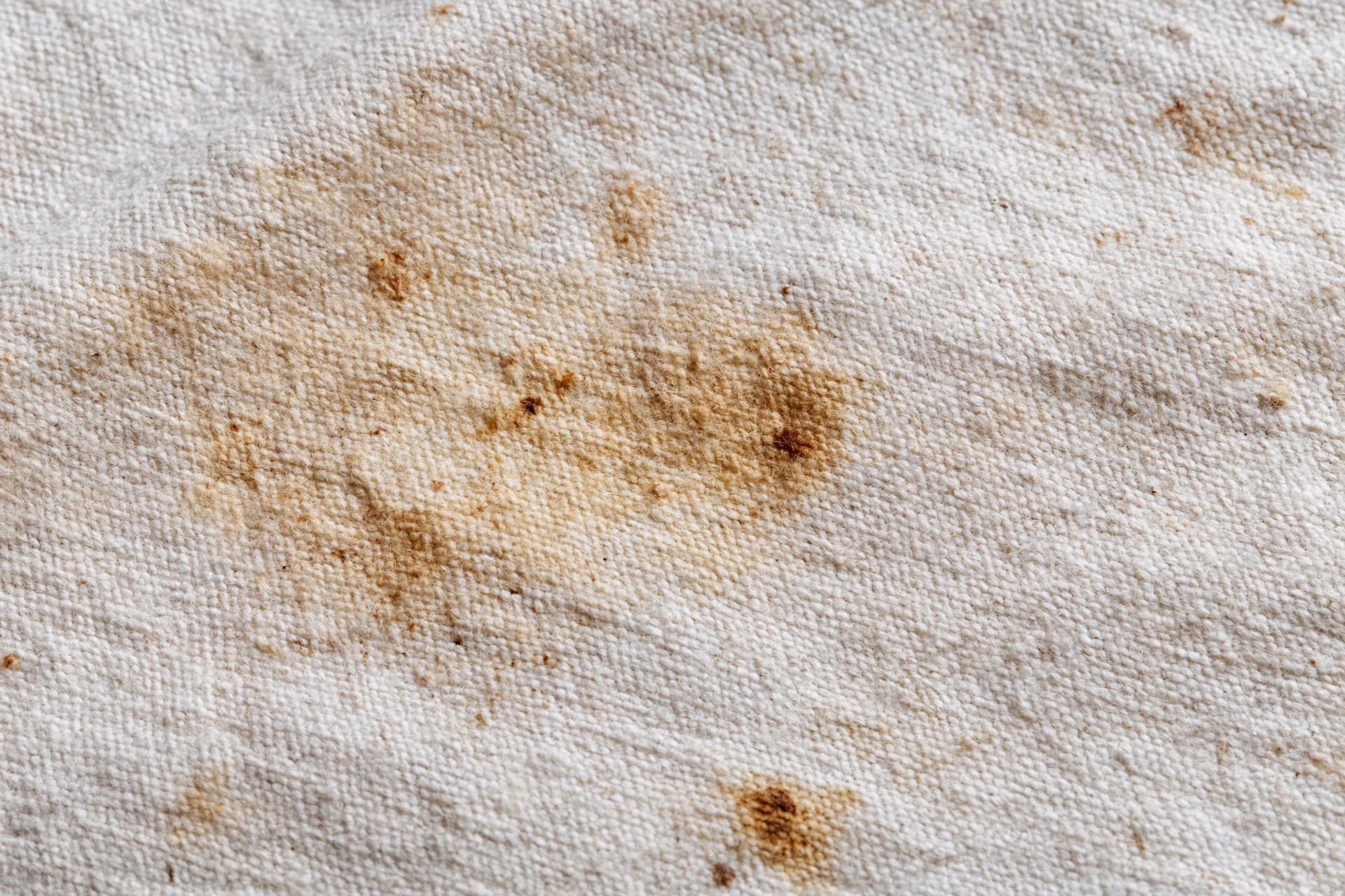 Close-up of stained natural linen canvas fabric with visible weave and brown discoloration