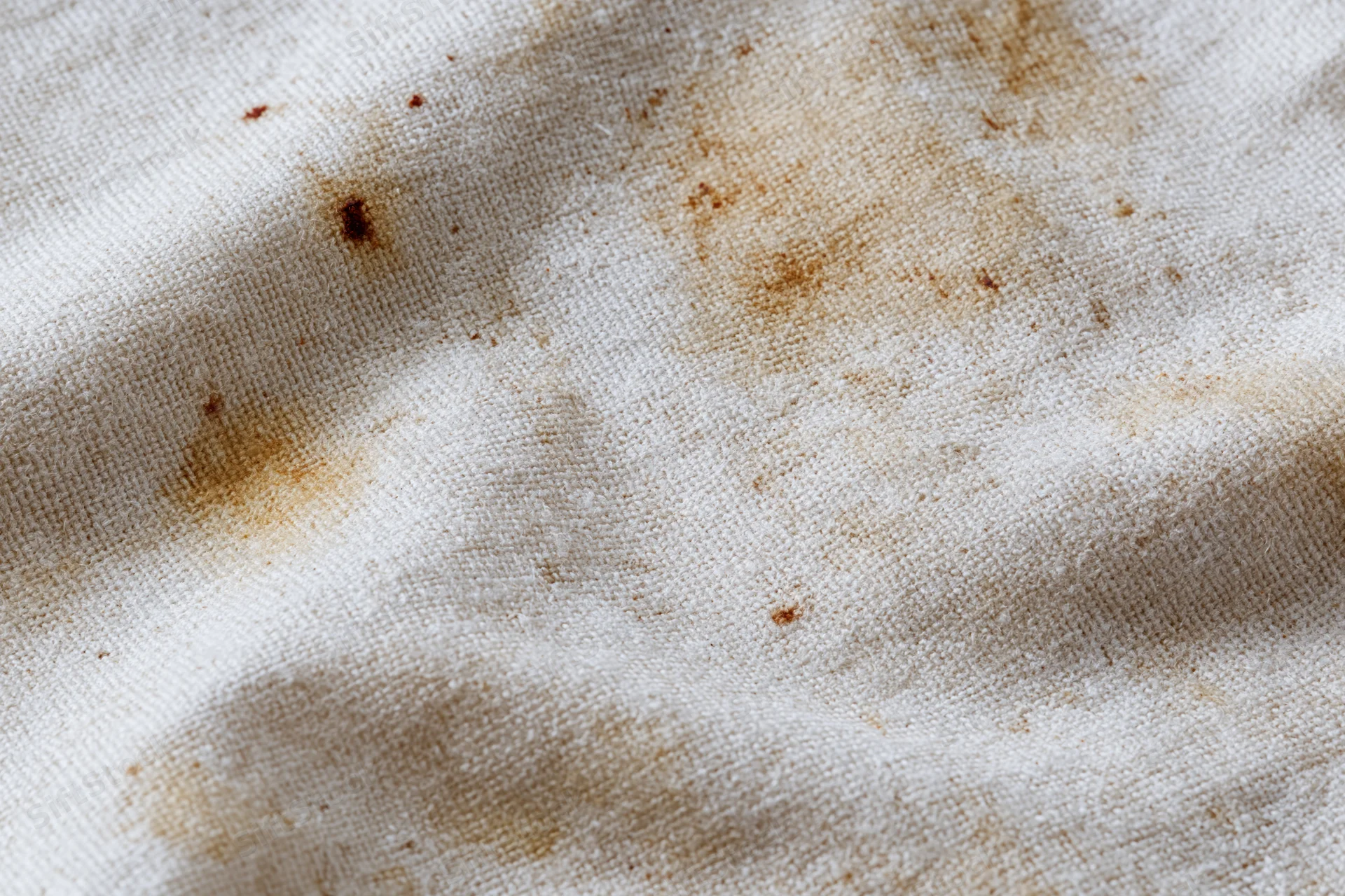 Close-up of stained natural linen canvas fabric with brown coffee or tea spills and visible weave texture