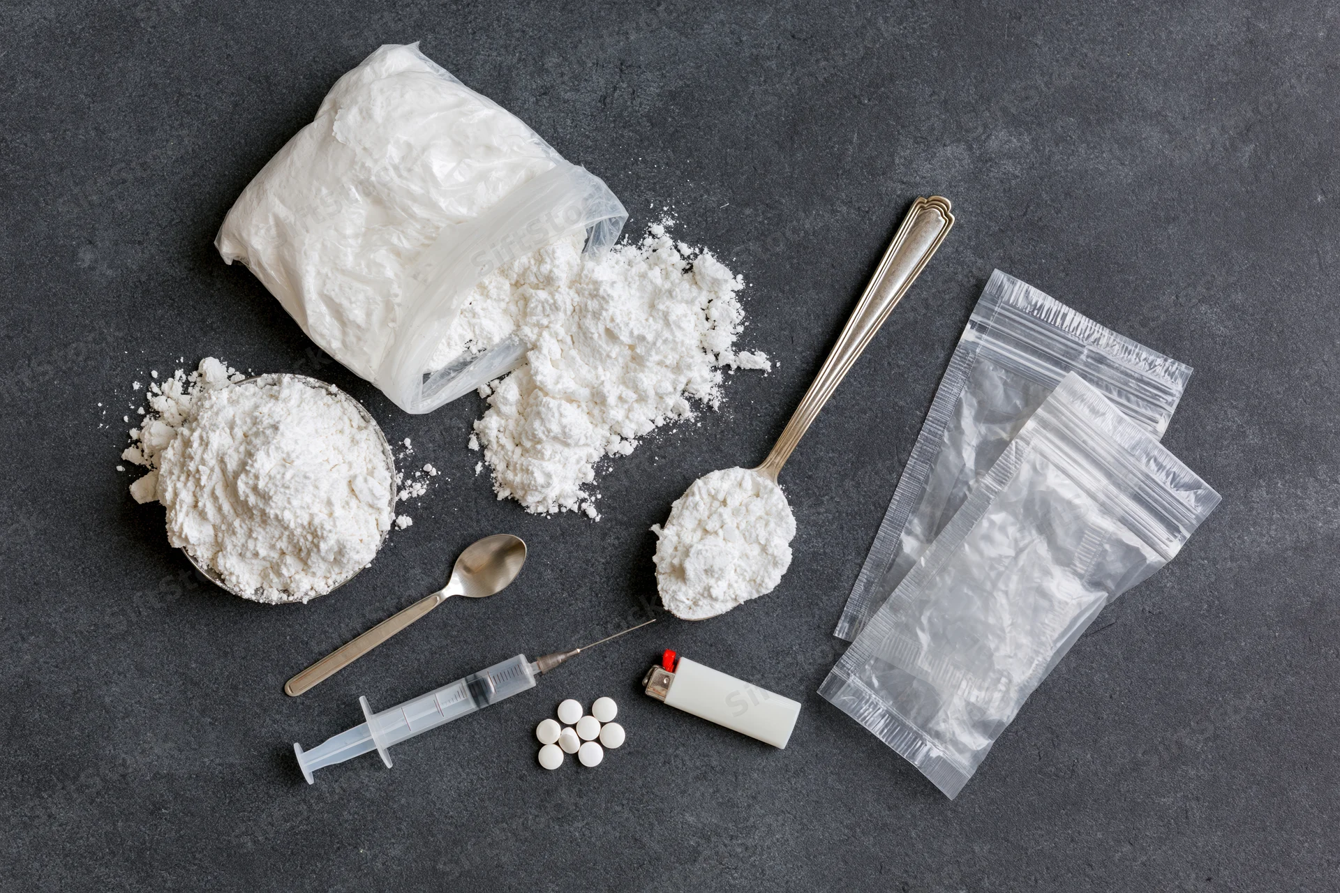 White powder and drug paraphernalia arranged on dark surface in flat lay view