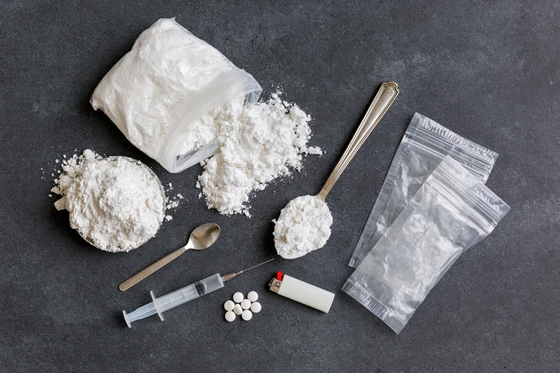 White powder and drug paraphernalia arranged on dark surface in flat lay view