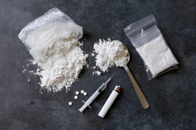 White powder and drug paraphernalia arranged on dark surface