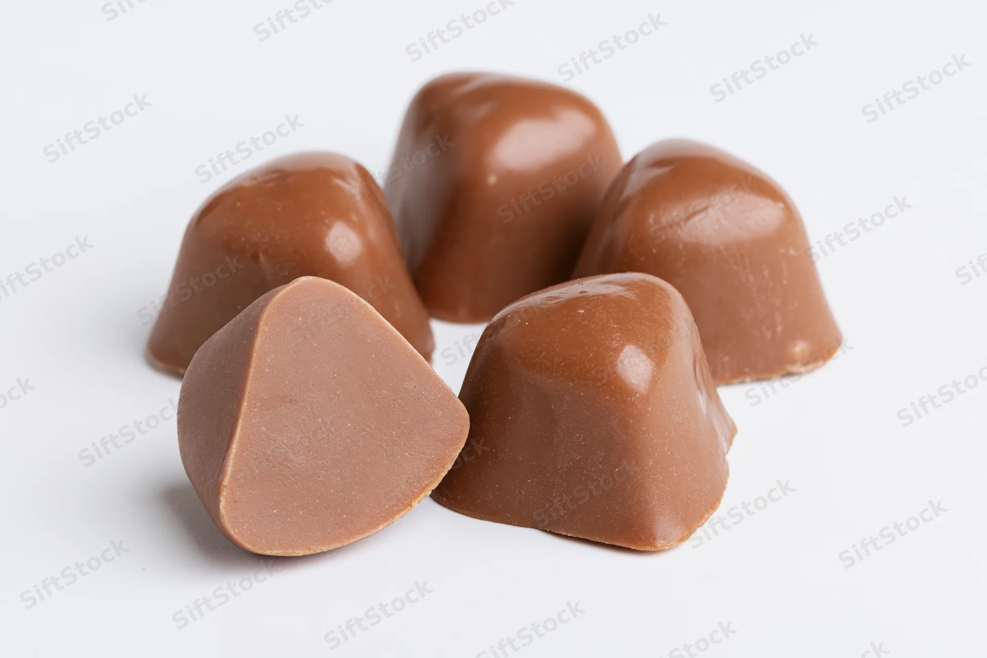 Milk chocolate caramel candies arranged on white surface