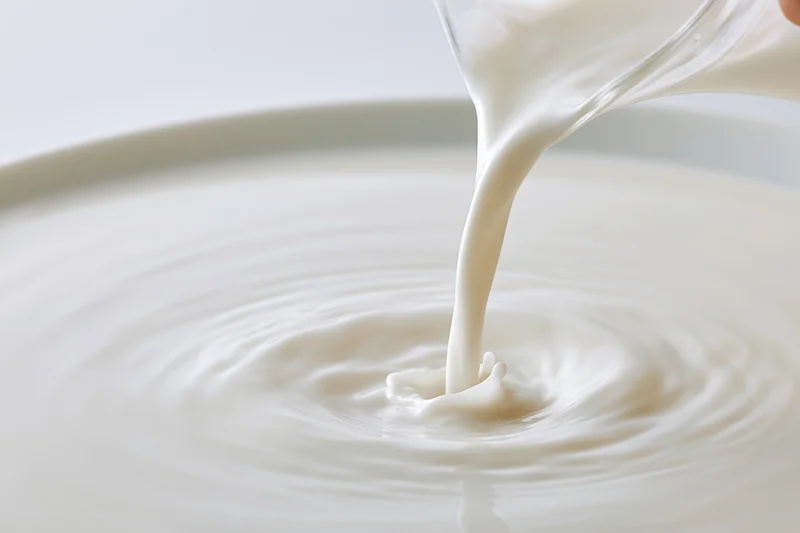 Milk pouring from a glass jug into a white bowl creating ripples