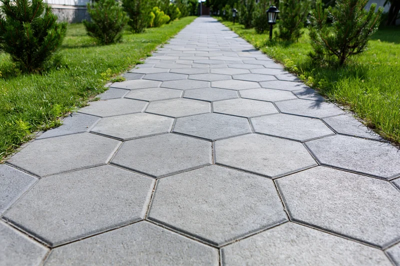 Hexagonal grey stone pathway stretching through a green lawn bordered by shrubs and lamps