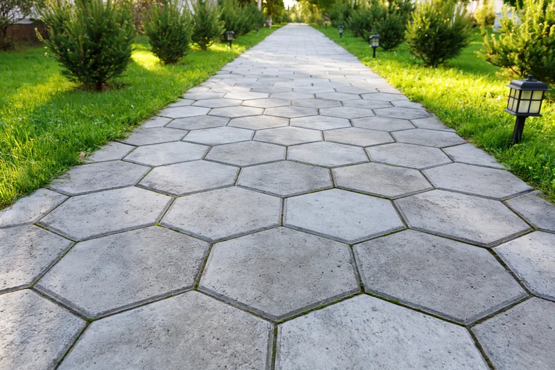 Hexagonal stone pathway stretching through a grassy garden with shrubs and lanterns on either side