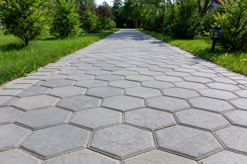 Hexagonal grey stone pathway stretching through a green garden with shrubs and lawn on either side