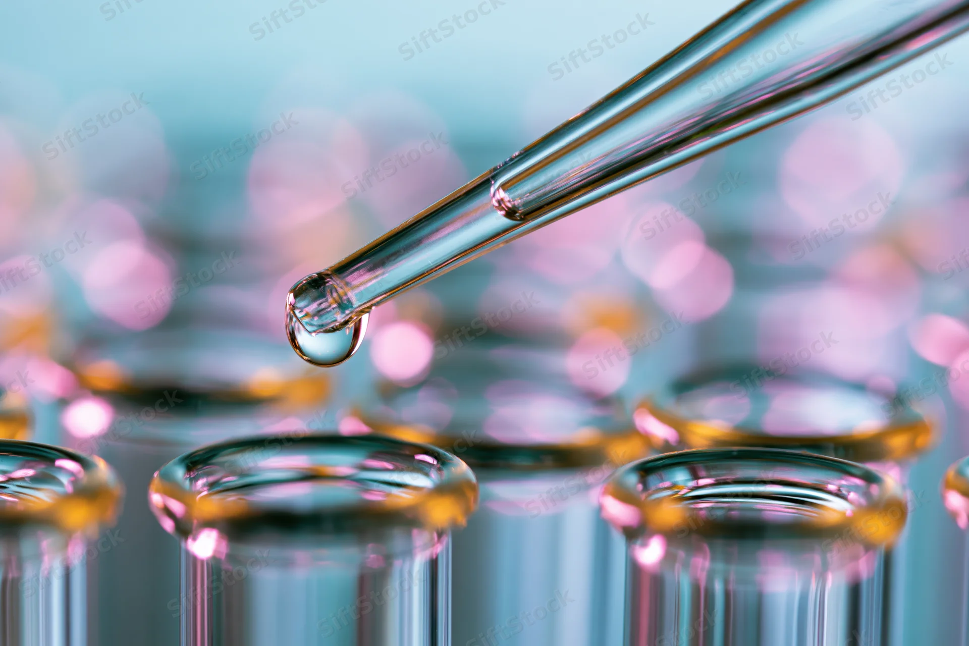 Glass pipette releasing a droplet over a row of test tubes in a lab setting