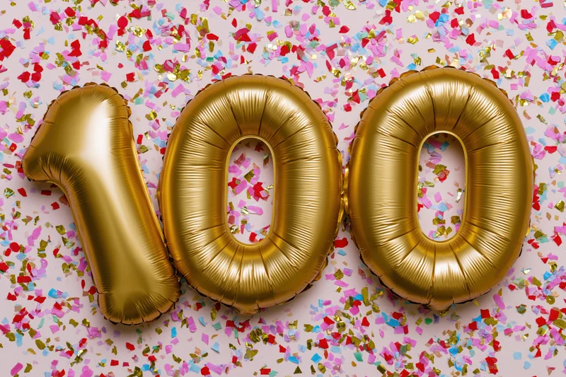 Gold foil number balloons spelling 100 on a surface covered with colorful confetti