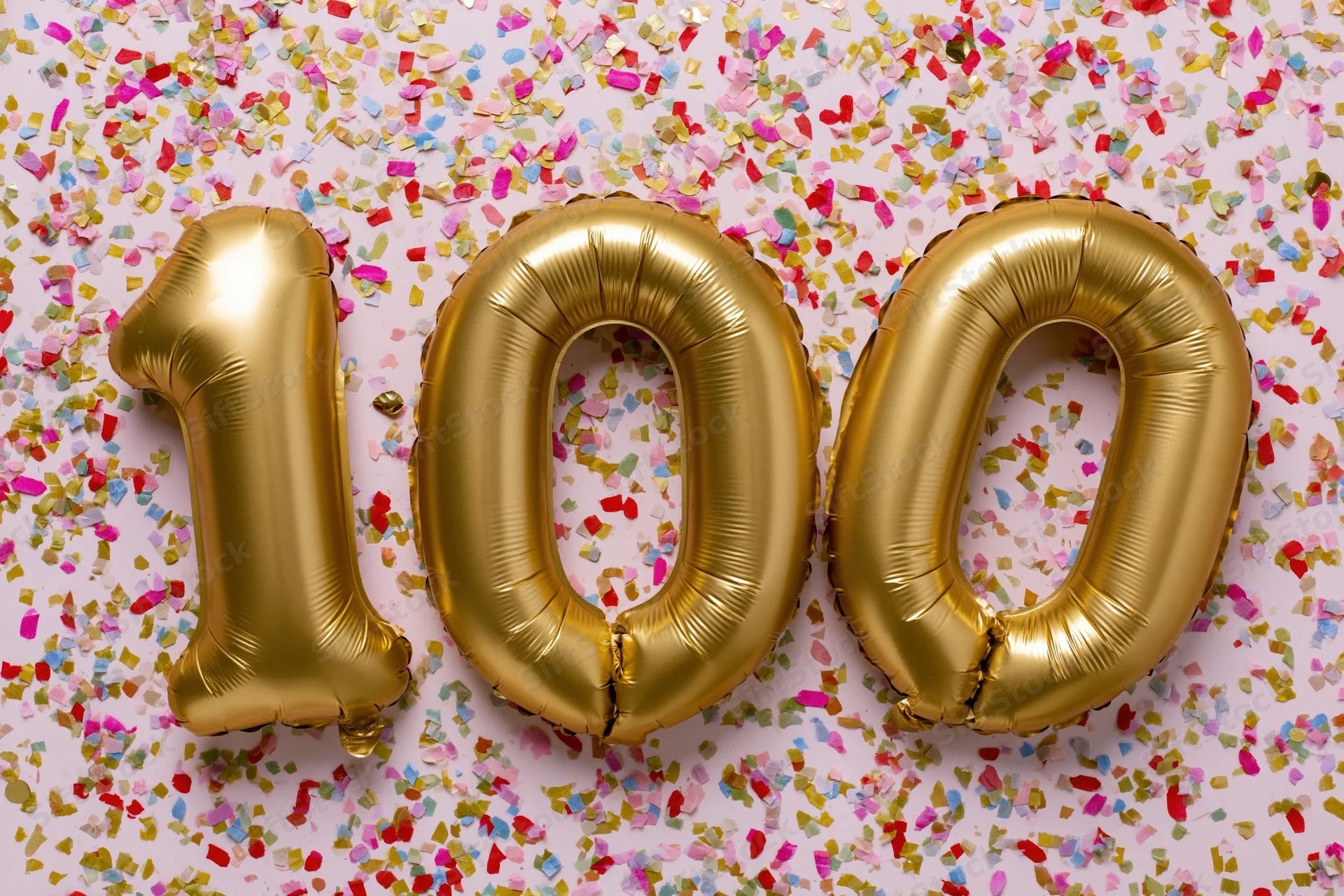 Gold foil number balloons spelling 100 on a confetti-covered surface