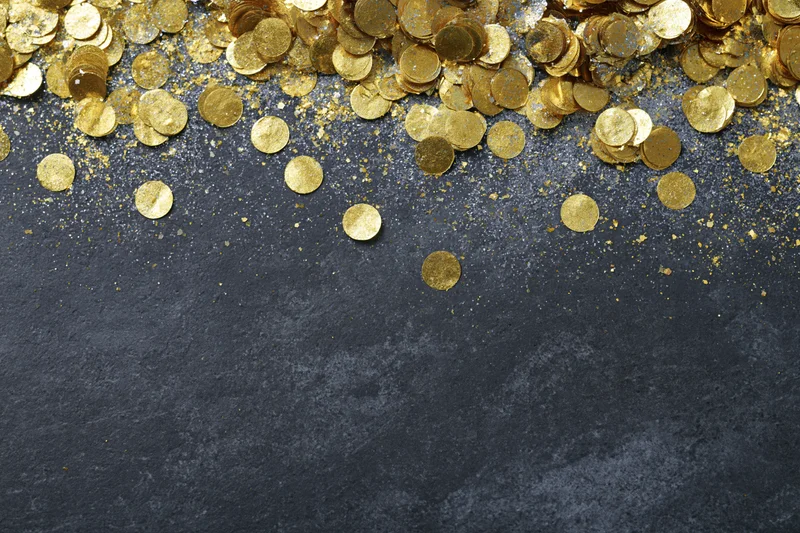 Gold metallic confetti and glitter scattered across dark textured surface with copyspace below