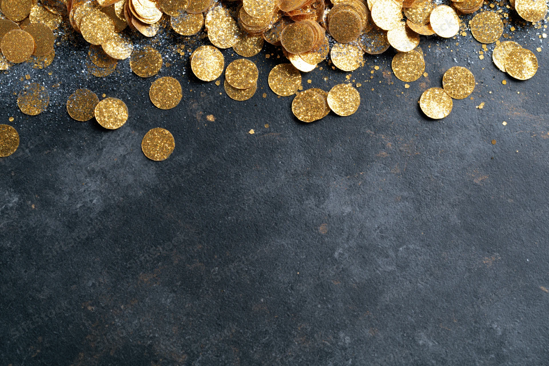 Gold metallic confetti and glitter scattered across dark textured surface with copyspace below